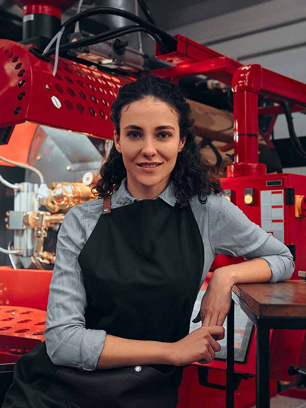 photo of female coffee roaster in front of a Toper Roaster next to paragrpah about how working with a good coffee roasting equipment broker like Coffee Equipment Pros can help