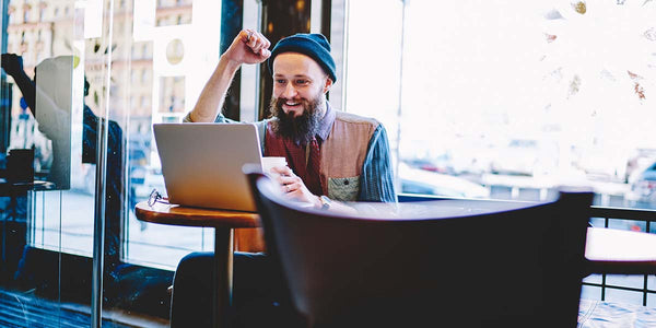 Man in coffee shop looking at laptop excited representing excitement when successfully financed by Coffee Equipment Pros